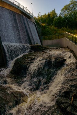 Arkasında büyüleyici bir köprü olan, yemyeşil ve berrak mavi bir gökyüzünün altındaki şelalenin resimsel bir görüntüsü.