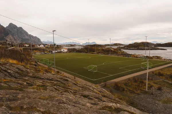 Norveç 'teki Henningsvaer futbol stadyumunun arka planında deniz ve adalar var. Lofoten Adaları 'ndaki futbol sahasında kayalar, taşlar ve su, panoramik manzara.