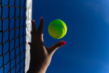 Kadın tenis topunu kalenin yanındaki gökyüzüne fırlatıyor.