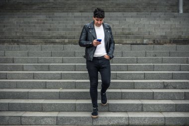 Koyu renk saçlı bir adam akıllı telefondan yazı yazarken merdivenlerden kafa kafaya iniyor.