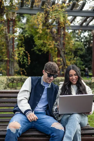 portrait vertical couple latin girl caucasian boy college students with laptop and headphones sitting on a university bench