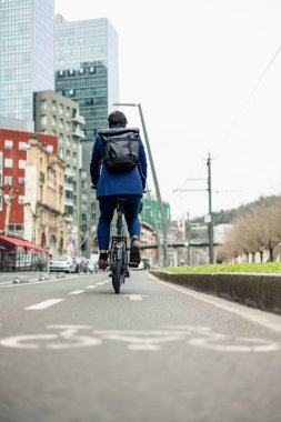 dikey portre bir iş adamı resmi olarak bisiklet pedalına basıyor şehir manzarasında bisiklet şeridinde, güvenli ve sürdürülebilir bir yolculuk için kask ve sırt çantasıyla donatılmış.