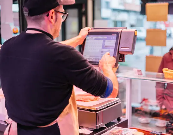 A cashier, seen from behind, is processing a customer\'s purchase using a modern digital cash register in a retail store. The scene depicts the checkout moment at the cash counter, where the transaction is completed efficiently and accurately