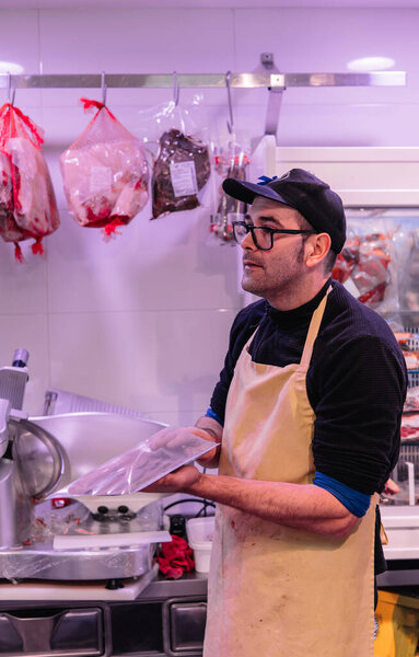 Vertical portrait In this bustling scene captured at the local butcher shop, a skilled butcher wearing a striped apron and protective glasses is meticulously packaging a freshly cut piece of meat. The essence of quality and craftsmanship is palpable
