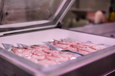 Paketleme makinesindeki vakumlu tavuk göğsüne yakın çekim. Sahne, et ürünlerinin tazeliğinin korunmasına ve raf ömrünün uzatılmasına yardımcı olan ve tüketiciler için kalitenin sağlanmasına yardımcı olan vakum mühür sürecini vurguluyor.