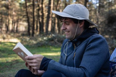 Mutlu maceracı, ormanın derinliklerinde çadırının önünde oturmuş, doğanın ortasında kitap okumaktan zevk alıyor.