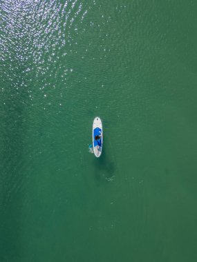 Dikey merkezî manzara kızı mavi küreğiyle denizde kürek çekiyor, sakin bir su sporu ve açık hava aktivitesinin keyfini çıkarıyor.