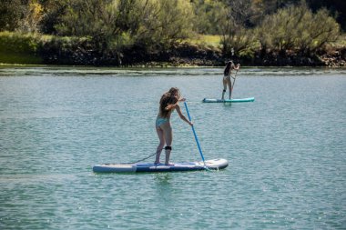 Güneşli bir yaz gününde güneşli bir gölde, açık hava su sporları ve eğlence aktivitelerinden keyif alırken arkadan görülen çok kültürlü, bikinili kadınlar.