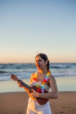 Dikey çok kültürlü genç bir kadın güzel bir yaz günbatımında ukulele çalmayı seviyor. Huzurlu bir atmosfer yaratıyor okyanus dalgalarıyla harmanlanan müziğin rahatlatıcı sesiyle.