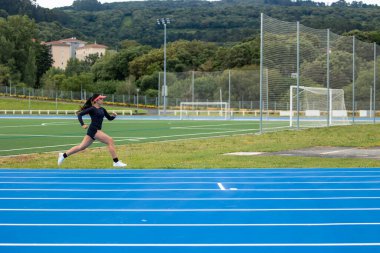 Telif alanı, vizörlü Latin kadın koşucu mavi bir atletizm pistinde hızla koşuyor. Bu dinamik görüntü, pistte yarışan atletin hızını ve kararlılığını yakalar.