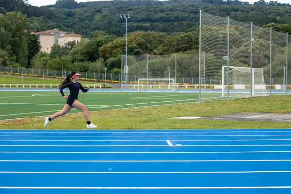 Telif alanı, vizörlü Latin kadın koşucu mavi bir atletizm pistinde hızla koşuyor. Bu dinamik görüntü, pistte yarışan atletin hızını ve kararlılığını yakalar.