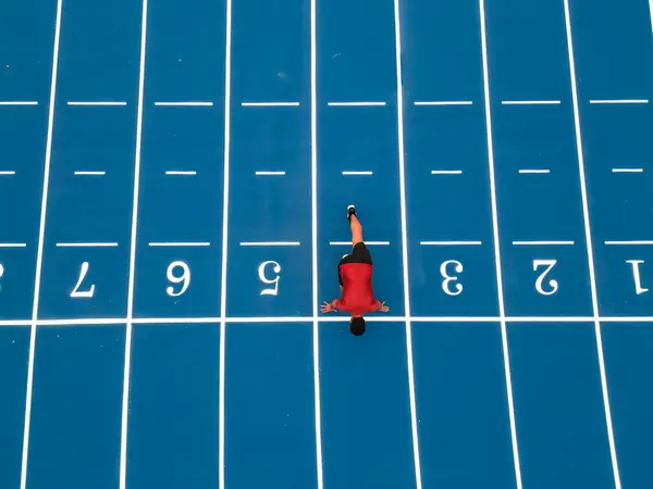 Hava aracının yakaladığı kuş bakışı görüntü mavi atletizm pistinde eğitime başlamak üzere çömelmiş bir koşucuyu gösteriyor..