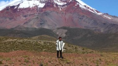 Geleneksel panço giyen Latin adam Ekvador 'da 6,263 metrede bulunan görkemli Chimborazo volkanı önünde poz veriyor. Sahne, bölgenin zengin kültürel mirasını yansıtıyor.