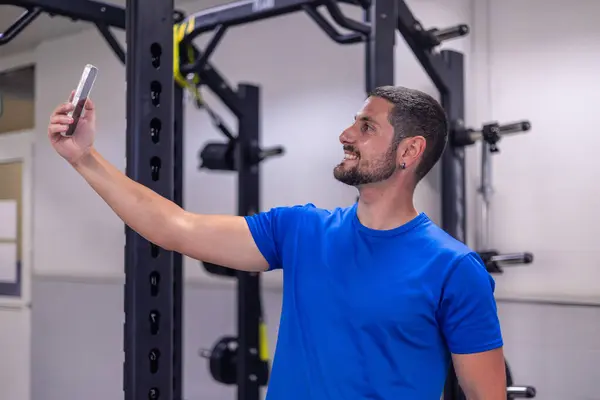 stock image smiling fitness sportsman takes a selfie with his smartphone during his gym workout. This image captures the modern trend of documenting fitness progress and sharing workout experiences