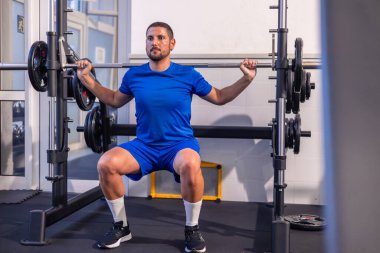 Genç fitness sporcusu, beden eğitimi rutini sırasında çok güçlü bir makine kullanarak ağırlık kaldırırken odaklanmış ve kararlı bir şekilde görülüyor..