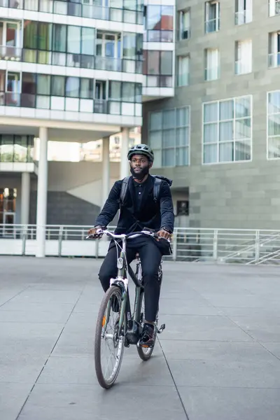 Stock image vertical African American black businessman pedaling eco-friendly with his electric bike on the way to work. It highlights sustainable urban mobility and professional commitment