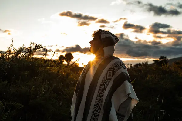 stock image multiracial Latino man wearing a traditional poncho poses against the backdrop of the Ecuadorian Andes during a stunning sunset. shows the cultural and natural beauty of the high-altitude landscape