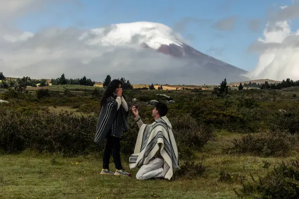 Stock image multiracial young man wearing a traditional poncho is proposing to his Latina girlfriend in front of the iconic Cotopaxi Volcano, situated in the Ecuadorian Andes