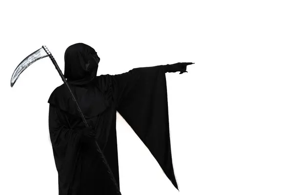 stock image The grim reaper, dressed in a Halloween costume with a dark cloak, holds a scythe in one hand and points ominously towards empty copyspace with the other white background