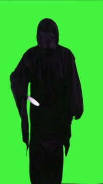 Dikey Azrail, Cadılar Bayramı kostümü giyip elinde bıçak tutarken yeşil ekran arka planına karşı boynu kesmekle tehdit ediyor.