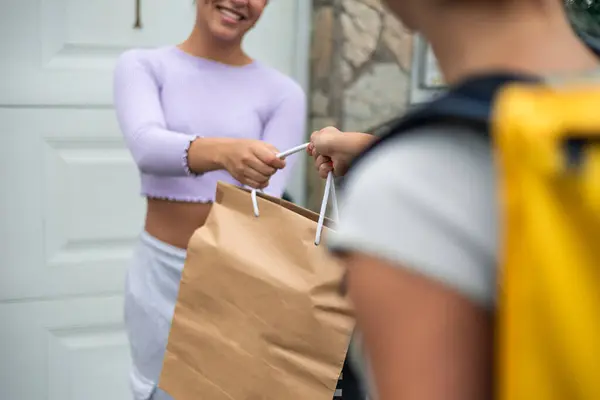 stock image closeup food delivery girl, viewed from behind, is delivering an order to an unrecognizable customer at their doorstep. The scene focuses on the delivery process