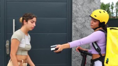 Müşteri, elektrikli scooterla müşterinin evine gelen yemek dağıtım kızına akıllı telefonla ödeme yapıyor. Kusursuz ödeme süreci ve teslimat etkileşimini yakalar