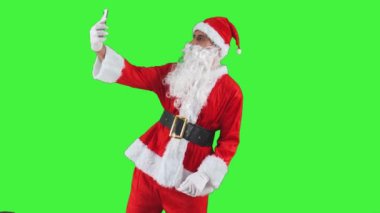 Noel Baba akıllı telefonuyla selfie çekerek eğlenceli bir anı yakalıyor. Neşeli ifade ve ikonik kırmızı elbise sahneyi neşeli ve neşeli krom anahtar yapar.