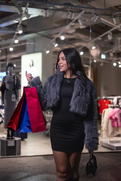 Dikey genç Latin kadın geceleri elinde çeşitli moda mağazalarından alınmış alışveriş çantalarıyla şehirde dolaşıyor. Şehrin ışıldayan ışıkları onun heyecanını yansıtıyor.
