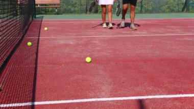 Tenis kıyafeti giymiş yaşlı bir çiftin tenis kortundaki kameraya doğru emin adımlarla yürürken bacakları yakın plan çekimde. Raketlerini tutuyorlar ve aktif bir yaşam tarzı sergiliyorlar.