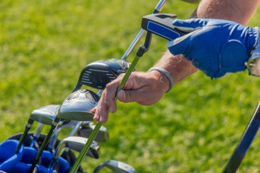Kıdemli golfçünün elleri golf çantasından golf sahasındaki bir sonraki atış için golf sopasını dikkatlice çıkarır.