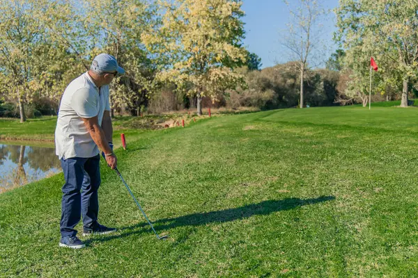Copyspace yaşlı golfçüsü golf sahasında gölün kenarında duran yeşil bayrağa doğru topa vurmak için sopasını sallarken görülüyor.