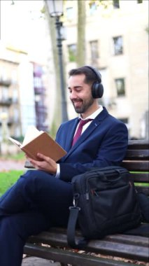 dikey iş adamı iş gününe ara veriyor, finans bölgesinde bir bankta oturuyor, kulaklıklarıyla müzik dinlerken kitap okuyor.