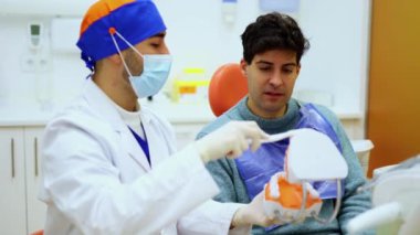 Diş hekimi bir hastaya düzgün diş fırçalama tekniklerini anatomik çene modeli kullanarak açıklıyor. Oturumda oral sağlık için temel diş bakımı ve hijyen uygulamaları vurgulanıyor