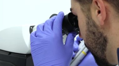 Yakın plan laboratuvar teknisyeni mor eldivenli örnekleri mikroskopla inceliyor, parlak, beyaz bir laboratuvar ortamında bilimsel araştırmalar yapıyor.