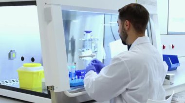 Laboratuvar teknisyeni laminar akış kabini içindeki test tüplerini dikkatlice kontrol ederek, bilimsel araştırma veya tıbbi test prosedürleri için steril bir ortam sağlıyor.