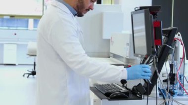 Eldiven ve laboratuvar önlüğü giyen laboratuvar teknisyeni, modern ve temiz bir laboratuvar ortamındaki bir bilgisayarda analiz için örnekleri kaydetmek için barkod tarayıcısı kullanıyor.