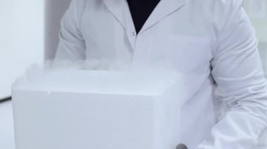 Steril laboratuvar ortamında kuru buz süblimleşme deneyi sırasında strafor konteynırından çıkan beyaz buharı tutan koruyucu giysi giyen bilim araştırmacısı.