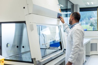 Beyaz önlüklü bilim adamı, modern bir bilim laboratuvarında araştırma için güvenli ve kontrollü bir ortam sağlamak için gaz başlığı ayarlarını ayarlıyor.