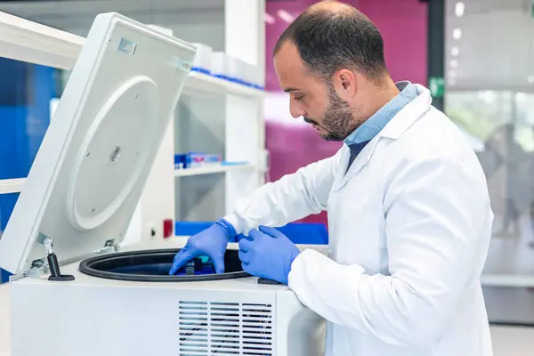 Laboratuvar önlüğü ve eldiven giyen tıp bilimadamı, bilimsel bir laboratuvarda farklı yoğunluktaki sıvıları ayırmak için kullanılan santrifüjün içine numune yerleştiriyor.