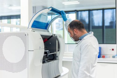 Laboratuvar önlüğü ve eldiven giyen bilim adamı, ileri düzey laboratuvar ekipmanlarını son teknoloji ürünü bir bilimsel tesiste tıbbi araştırma yapmak için açıyor.