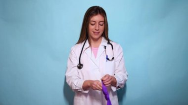 Mor cerrahi eldivenli kadın profesyonel hasta muayenesine hazır, steteskop takıyor açık mavi stüdyo arka planına karşı.