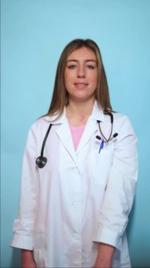 Beyaz laboratuvar önlüğü ve steteskop giyen dikey profesyonel kadın doktor. Mavi stüdyo ortamında dururken ilk yardım çantasını sunuyorum. Acil yardım öneriyorum.