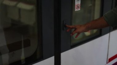 Tren kapısını açmak için düğmeye basan bir gezginin elinin yakın çekimi, binmeye hazır. Yolculuğun aksiyonunu yakaladığı an, 4k video