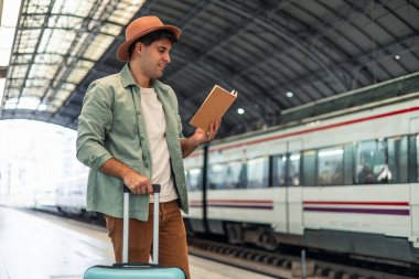 Tren istasyonunda beklerken kitap okuyan genç bir latin gezgin, elinde bir tramvay valizi, hareketli bir şehir ortamında seyahat ve tatilin özünü somutlaştırıyor.