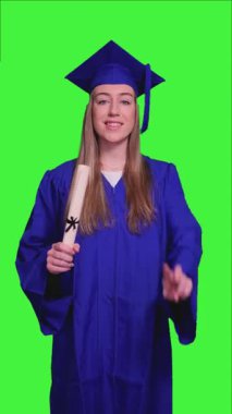 Mavi akademik önlük ve havan panosu giyen, elinde diploma tutan ve yeşil perde arkasını işaret eden, akademik başarı ve başarının somutlaştırıldığı dikey kadın mezunu.