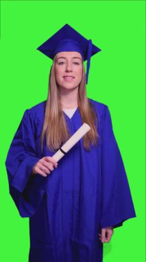 Mavi önlük ve havan panosu giyen genç öğrenci diplomasını tutuyor ve yeşil ekran arka planında farklı jestler yapıyor.