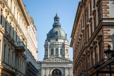 02 / 17 / 2024, Budapeşte. Aziz Stephen Bazilikası, çarpıcı bir Budapeşte simgesi, dar bir sokaktan görkemli bir şekilde yükseliyor, büyük kubbesini vurguluyor ve şehir manzarasına karşı karmaşık bir cephe oluşturuyor.