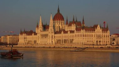 02-17-2025, Budapeşte. Macaristan Parlamento Binası 'na vuran altın günbatımı ışınları. Turist teknesi suda süzülürken Tuna Nehri 'ne yansıyor. Budapeşte 'nin ikonik şehir manzarasını sihirli akşam ışığında yakalamak