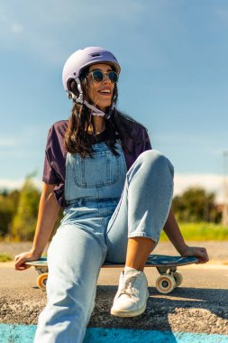 Pompa pistinde sörf yaparken gülümseyen bir kadın kask ve güneş gözlüğü takıyor, güneşli bir günde açık havada en sevdiği sporu yapıyor.