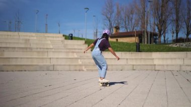 Parkta sörf antrenmanı yapan enerjik Latin sporcu kadın, günlük kıyafetler ve kaskla güneşli bir günün tadını çıkarırken dengesini ve koordinasyonunu sağlıyor.
